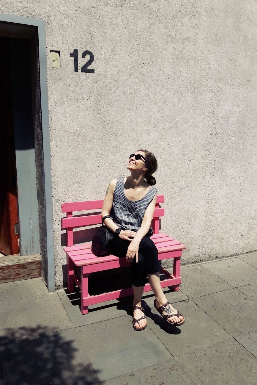 Jessica is sitting in a bright pink chair in front of Luis Barragan's home and studio in Mexico City.